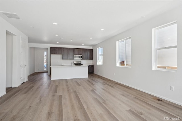 kitchen featuring a center island with sink, light hardwood / wood-style floors, dark brown cabinets, and stainless steel appliances