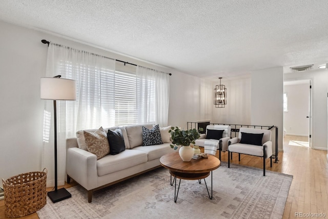 living room with a chandelier, a textured ceiling, and light hardwood / wood-style flooring