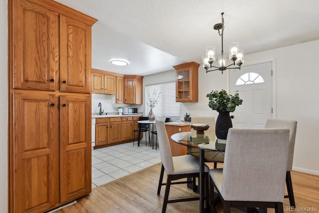 dining area featuring a notable chandelier, light hardwood / wood-style flooring, sink, and a textured ceiling