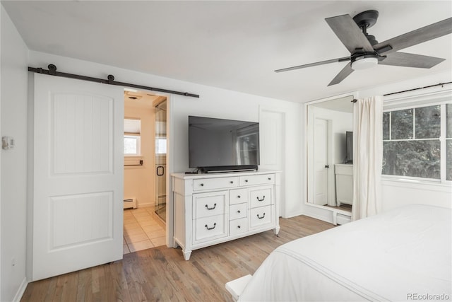 bedroom featuring light wood-style floors, ensuite bath, baseboards, a barn door, and a ceiling fan