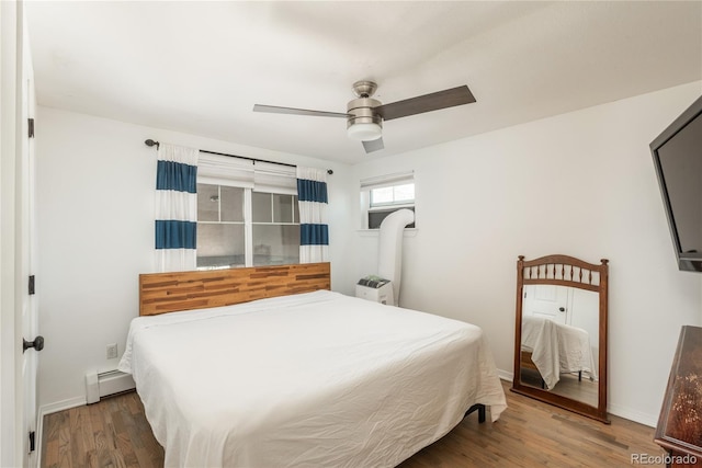 bedroom featuring baseboard heating, wood finished floors, a ceiling fan, and baseboards
