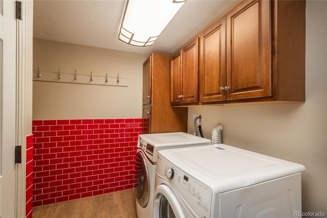 washroom with cabinet space, wood finished floors, washer and dryer, tile walls, and a wainscoted wall