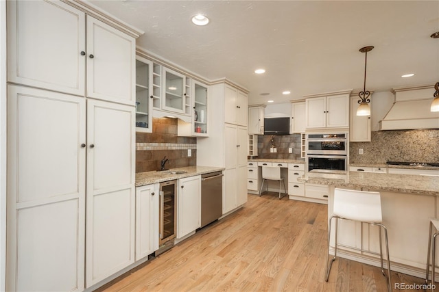 kitchen featuring appliances with stainless steel finishes, custom range hood, wine cooler, decorative backsplash, and a sink