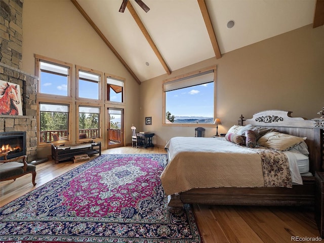 29548 Sunset Trl, Pine, CO 80470 - bedroom with a stone fireplace, wood finished floors, access to exterior, beam ceiling, and high vaulted ceiling