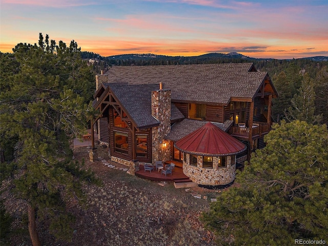 29548 Sunset Trl, Pine, CO 80470 - back of house at dusk with stone siding, a chimney, a balcony, and a deck