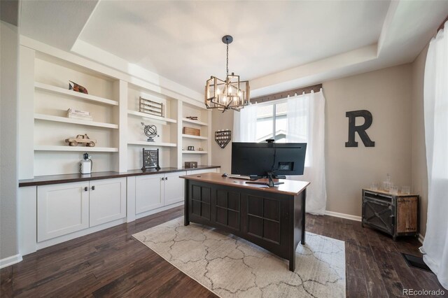 home office with a notable chandelier, built in shelves, a raised ceiling, and dark hardwood / wood-style flooring