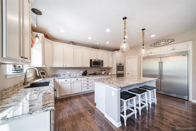 kitchen with appliances with stainless steel finishes, sink, decorative light fixtures, white cabinetry, and a kitchen island