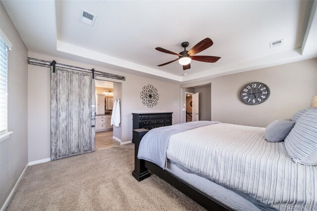 carpeted bedroom featuring ceiling fan, a barn door, ensuite bath, and a tray ceiling