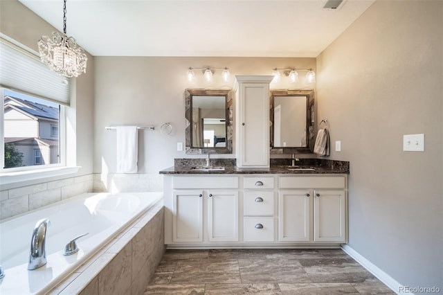 bathroom featuring tiled tub, vanity, and an inviting chandelier