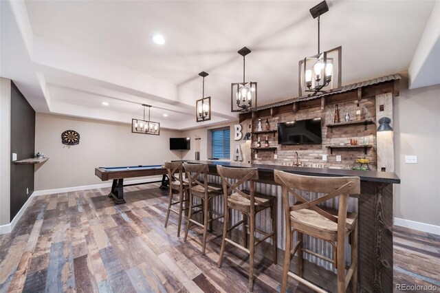 bar featuring sink, dark wood-type flooring, hanging light fixtures, and a raised ceiling