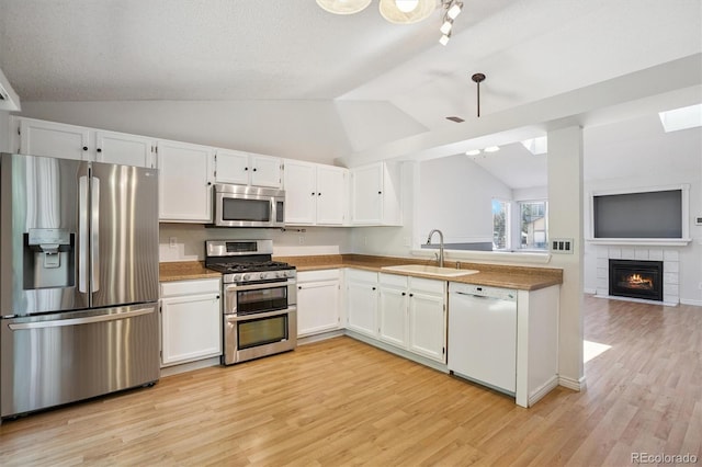 4947 S Espana Way, Centennial, CO 80015 - kitchen with appliances with stainless steel finishes, lofted ceiling, light wood-style flooring, a tile fireplace, and white cabinets