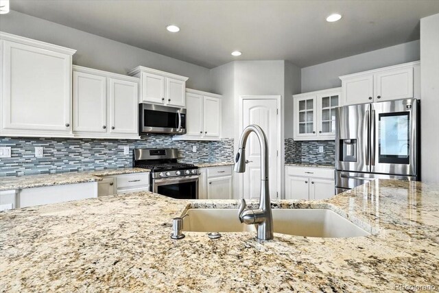 8205 Birch Tree Loop, Colorado Springs, CO 80927 - kitchen with appliances with stainless steel finishes, white cabinets, light stone counters, backsplash, and glass insert cabinets