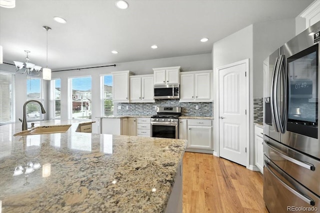 8205 Birch Tree Loop, Colorado Springs, CO 80927 - kitchen with stainless steel appliances, backsplash, white cabinets, light wood-style flooring, and decorative light fixtures