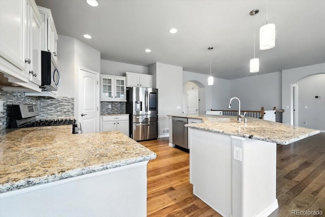 8205 Birch Tree Loop, Colorado Springs, CO 80927 - kitchen with arched walkways, stainless steel appliances, a center island with sink, backsplash, and recessed lighting