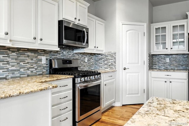 8205 Birch Tree Loop, Colorado Springs, CO 80927 - kitchen with stainless steel appliances, white cabinets, light wood finished floors, decorative backsplash, and glass insert cabinets