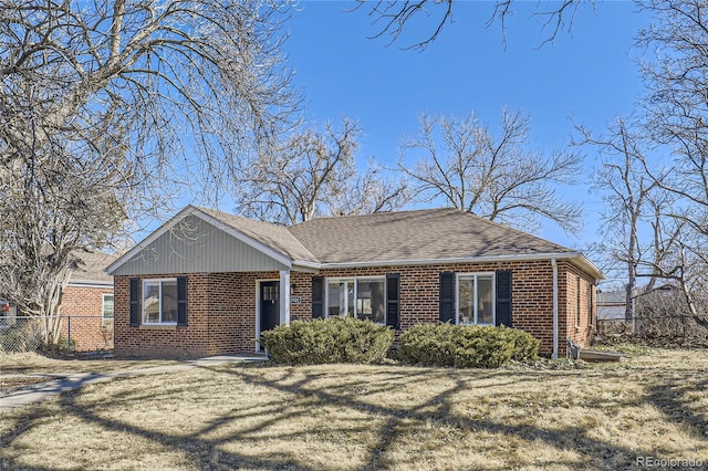 ranch-style home with a shingled roof, a front yard, fence, and brick siding