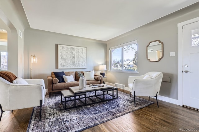 living room featuring a healthy amount of sunlight, visible vents, arched walkways, and wood finished floors