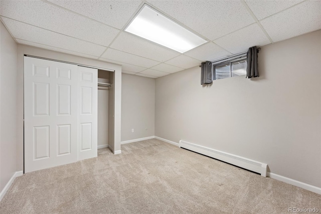 unfurnished bedroom with light carpet, a baseboard heating unit, a drop ceiling, and a closet