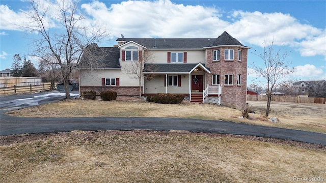 view of front of home featuring brick siding, fence, driveway, and a front yard