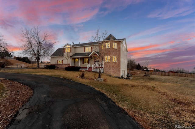 view of front of property with a porch, a lawn, fence, and driveway