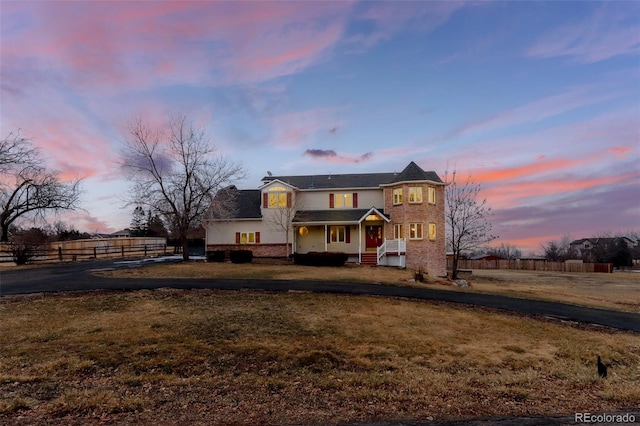 view of front of home featuring brick siding, fence, a front yard, and aphalt driveway