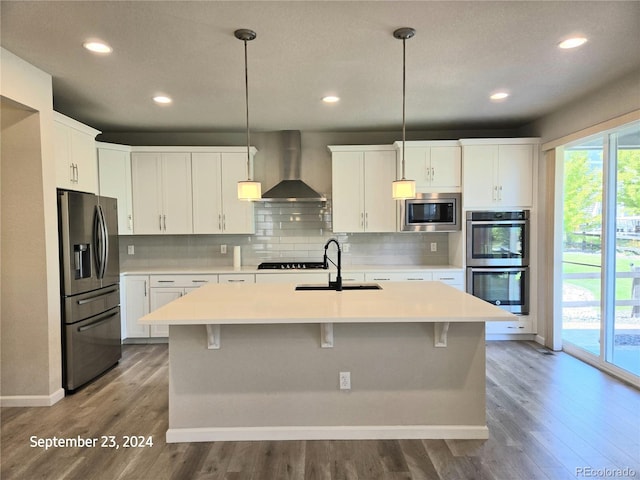 kitchen featuring hanging light fixtures, wall chimney exhaust hood, white cabinetry, and stainless steel appliances