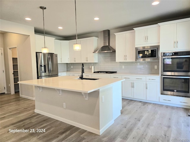 kitchen with sink, wall chimney range hood, stainless steel appliances, and white cabinets