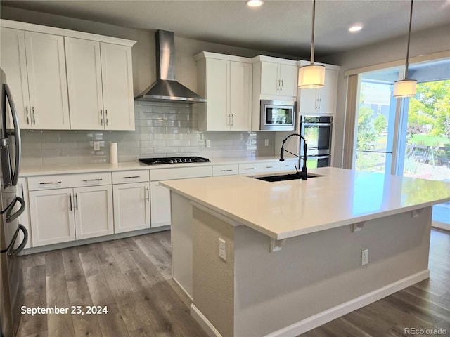 kitchen with appliances with stainless steel finishes, wall chimney exhaust hood, white cabinets, and decorative light fixtures