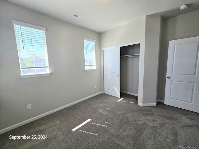 unfurnished bedroom with dark carpet, a closet, and multiple windows