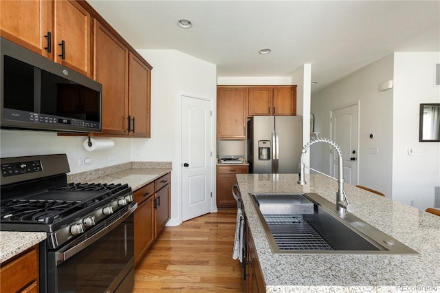 kitchen featuring light stone countertops, light wood-style floors, brown cabinets, a sink, and stainless steel appliances