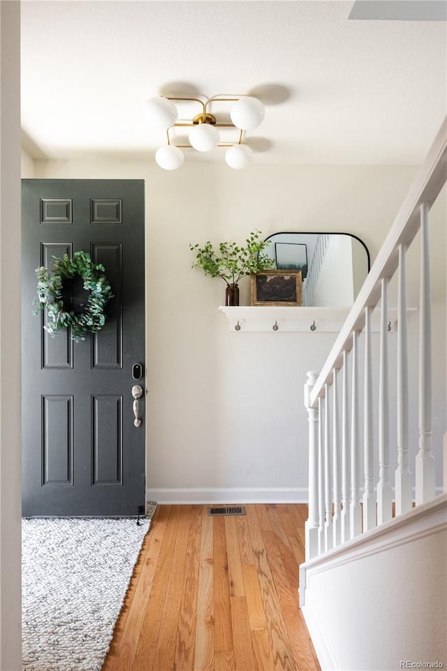 foyer entrance with visible vents, wood finished floors, stairway, baseboards, and a chandelier