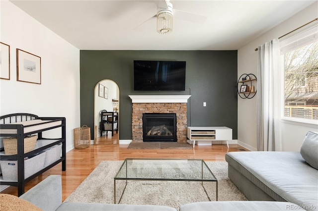 living area featuring ceiling fan, a fireplace, arched walkways, baseboards, and wood finished floors