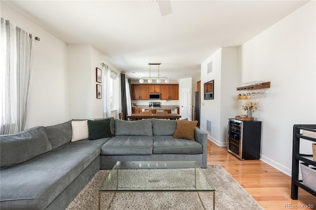 living room with baseboards, visible vents, a dry bar, and light wood finished floors