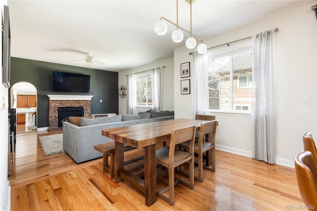 dining area featuring a fireplace, ceiling fan, baseboards, and light wood-type flooring