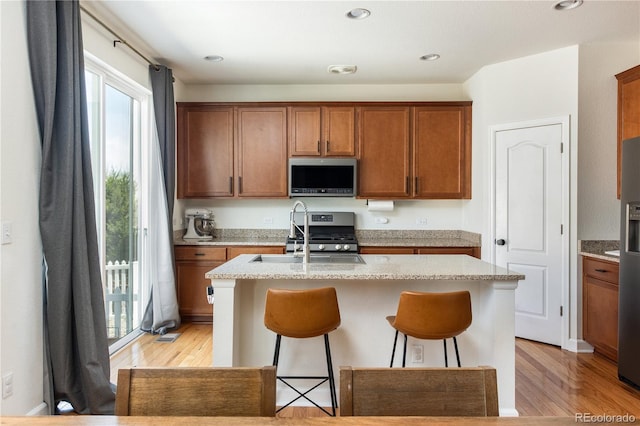 kitchen with a kitchen bar, a sink, light wood-style floors, stainless steel appliances, and an island with sink