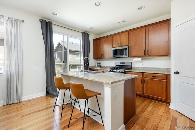 kitchen featuring a sink, light wood finished floors, a breakfast bar area, brown cabinetry, and stainless steel appliances