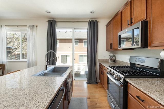 kitchen with a sink, appliances with stainless steel finishes, brown cabinets, and light wood-style flooring