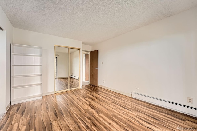 unfurnished bedroom with baseboard heating, wood finished floors, a textured ceiling, a closet, and baseboards