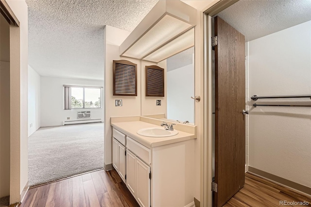 bathroom with a textured ceiling, a baseboard heating unit, vanity, and wood finished floors
