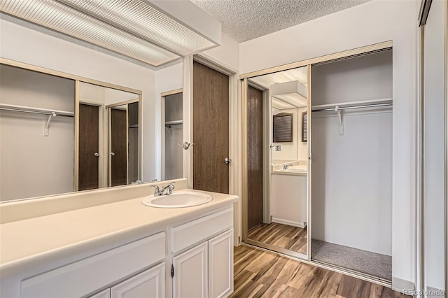 bathroom with a spacious closet, wood finished floors, vanity, and a textured ceiling