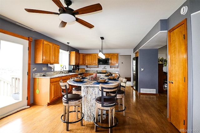 3530 Doolittle Rd, Monument, CO 80132 - kitchen with black microwave, brown cabinetry, light wood finished floors, a breakfast bar, and a center island