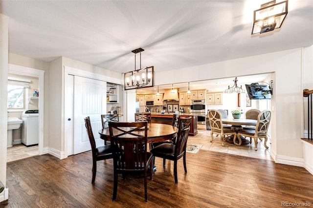 dining room featuring washer / dryer, light hardwood / wood-style flooring, and a chandelier