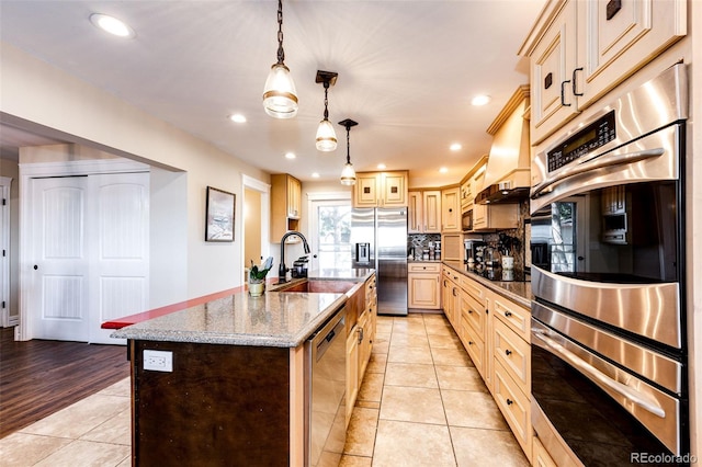 kitchen with sink, a kitchen island with sink, hanging light fixtures, stainless steel appliances, and light stone countertops