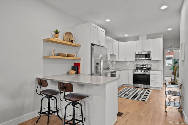 3003 California St, Denver, CO 80205 - kitchen featuring appliances with stainless steel finishes, decorative backsplash, light wood finished floors, a kitchen bar, and a peninsula