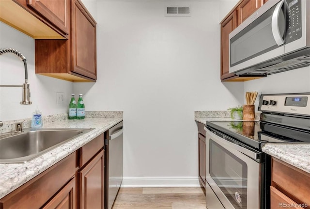 kitchen with light stone countertops, appliances with stainless steel finishes, sink, and light wood-type flooring