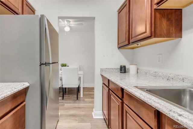 kitchen with ceiling fan, light stone countertops, stainless steel refrigerator, and light hardwood / wood-style flooring