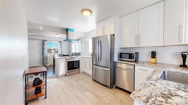 kitchen featuring wall chimney exhaust hood, appliances with stainless steel finishes, white cabinets, and backsplash