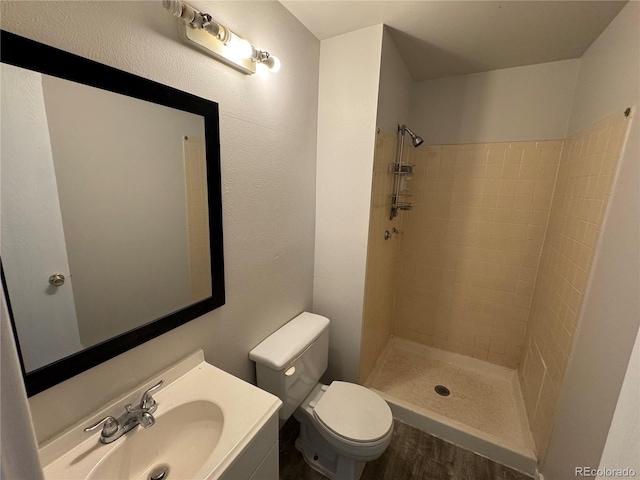 full bathroom featuring wood finished floors, a tile shower, toilet, and vanity