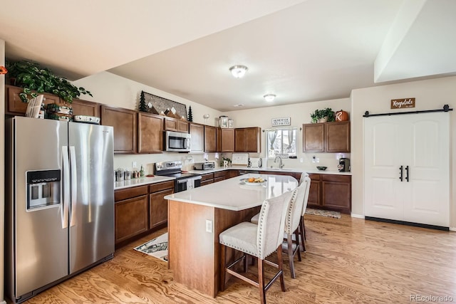 kitchen featuring a breakfast bar area, light wood-type flooring, light countertops, appliances with stainless steel finishes, and a sink