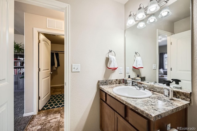 bathroom with a spacious closet, visible vents, vanity, and baseboards